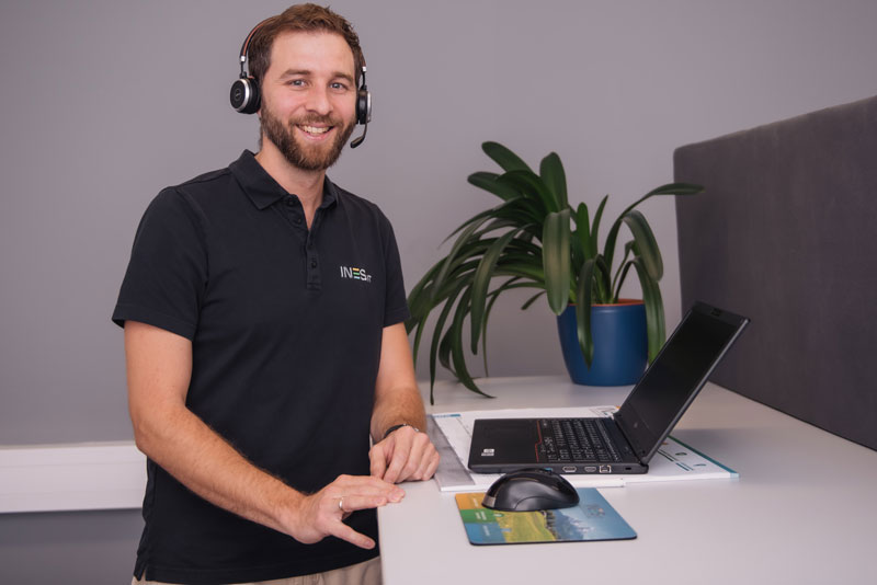 INES Mitarbeiter steht mit Headset am Schreibtisch